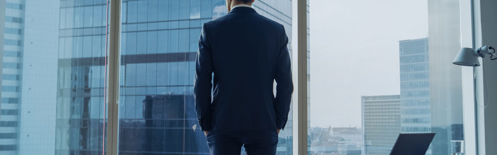 wealthy man staring out highrise corporate building